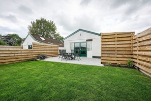 A house with a fenced backyard, a patio with a table and chairs, and a green door.