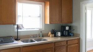 A kitchen with wooden cabinets, a double sink, a window with blinds, a coffee maker, and a knife block. - 7 Minute Walk to Kyle Field - Charming Cottage (College Station)