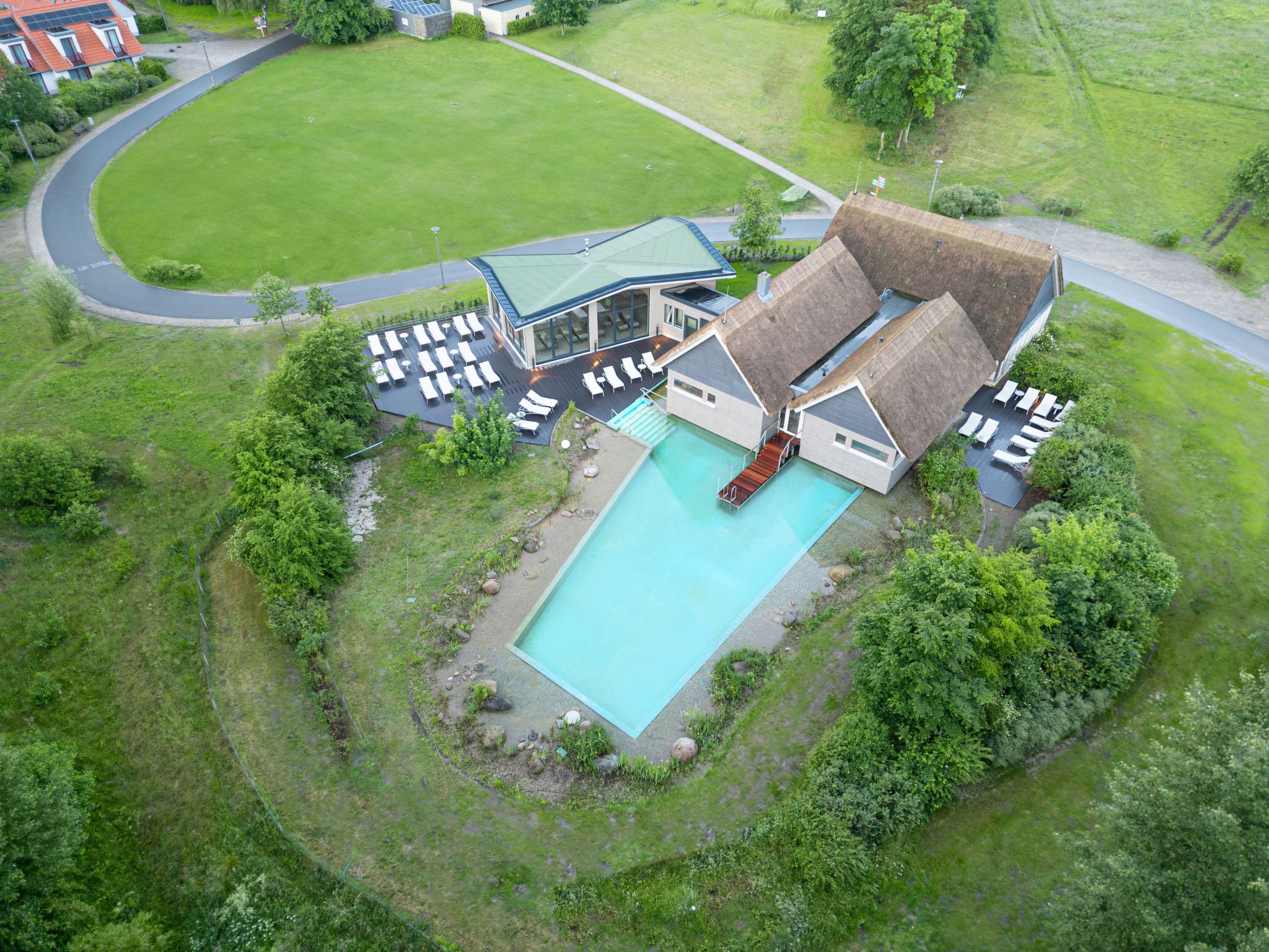 An aerial view of a resort with a swimming pool, sun loungers, and a covered outdoor area.