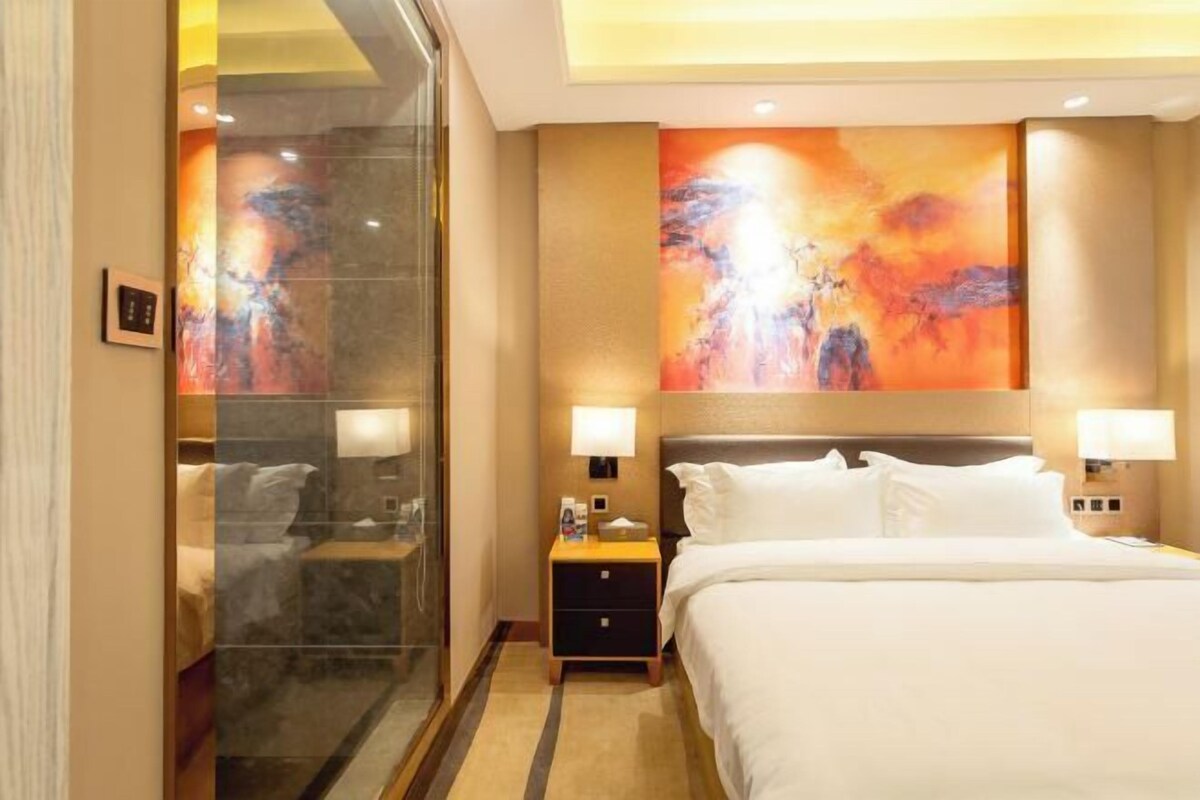A hotel room with a bed, nightstands, a glass shower enclosure, and two large abstract paintings on the walls.
