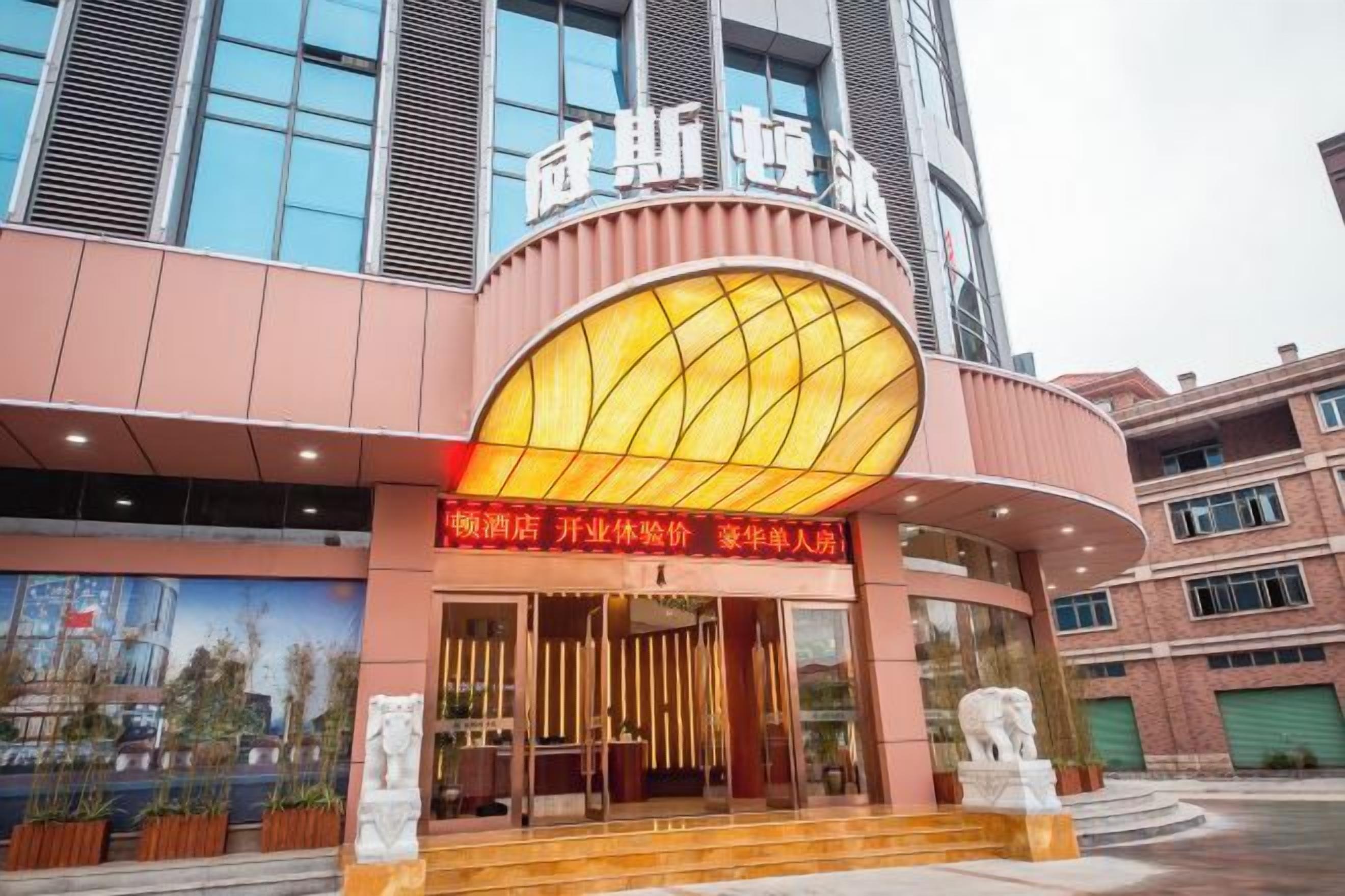 A hotel entrance with a large illuminated sign, a curved facade, and a statue in front.