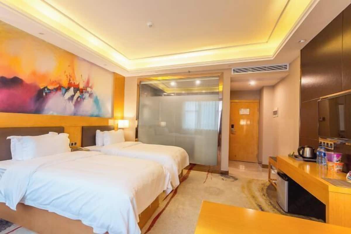 Ein Hotelzimmer mit zwei Betten, einem Schreibtisch, einem Fernseher und einem Bild an der Wand.