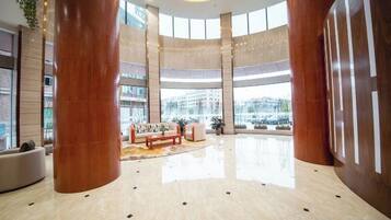 Un hall amplio con zona de estar central, pilares grandes y vistas al exterior.