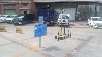 A parking lot with multiple cars, a blue parking sign, and a building with a garage door in the background.