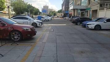 Un estacionamiento con varios autos estacionados a lo largo de la calle, edificios al fondo y un cielo despejado.