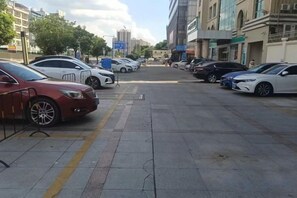 A parking lot with multiple cars parked along the street, buildings in the background, and a clear sky.