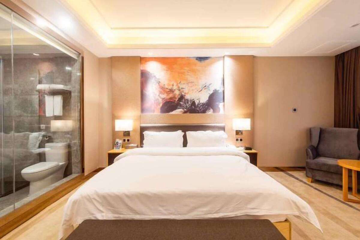 Ein Hotelzimmer mit einem großen Bett, einer Dusche mit Glastrennwand, einer Sitzecke mit Stuhl und Tisch sowie einem Bild an der Wand.