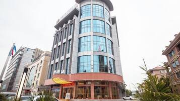 Un hotel de varios pisos con fachada curva, un restaurante visible en la planta baja y un estacionamiento al frente.