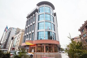 A multi-story hotel with a curved facade, a visible restaurant at the ground level, and a parking area in front. - Weisidun Hotel (Dongguan)