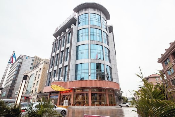 A multi-story hotel with a curved facade, a visible restaurant at the ground level, and a parking area in front. - Weisidun Hotel (Dongguan)
