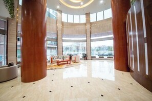 A spacious lobby with large wooden columns, a central seating area, and large windows offering views of the city.