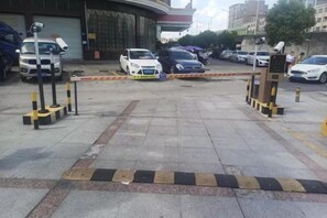 A parking lot with cars, a gated entrance, bollards, and a building in the background. - Weisidun Hotel (Dongguan)