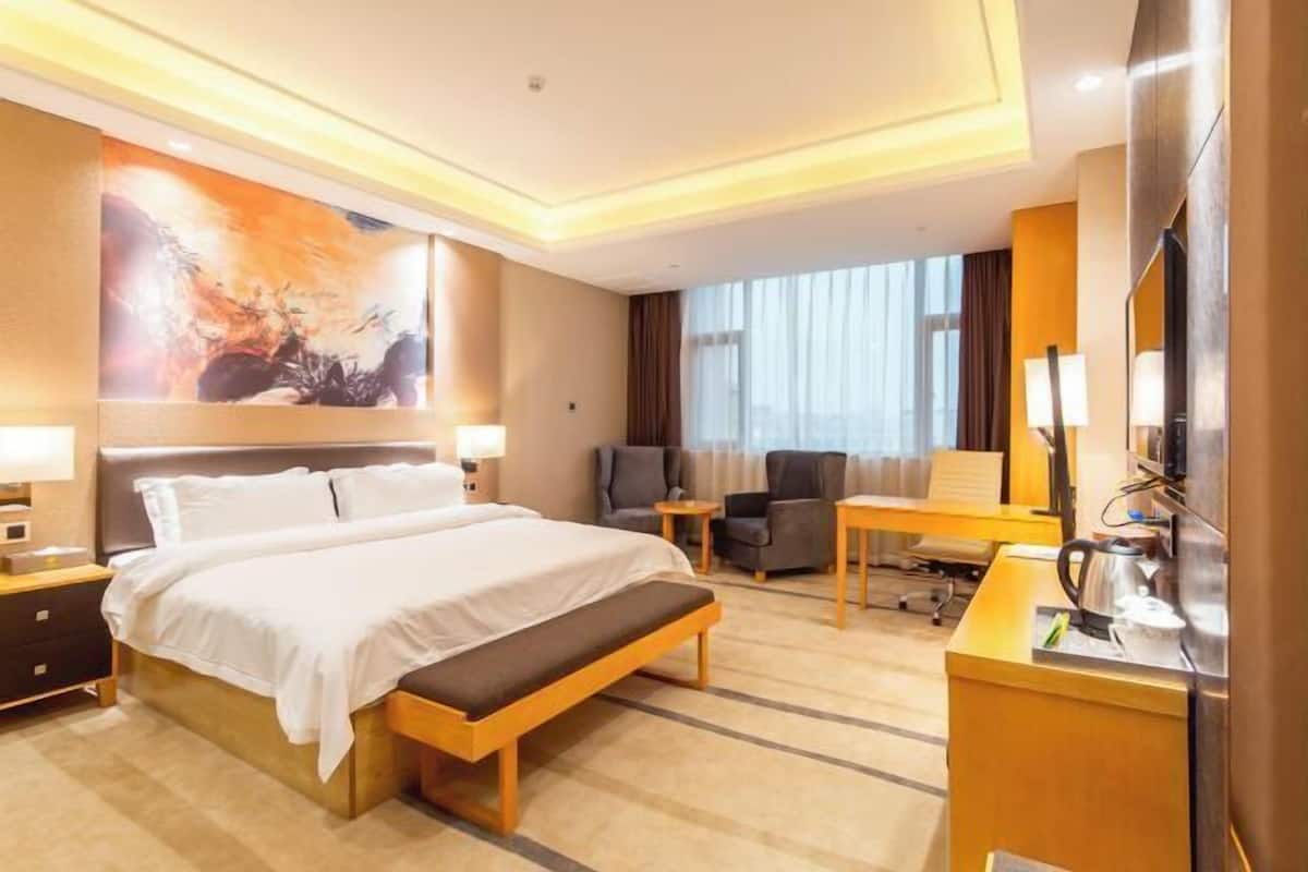 Ein Hotelzimmer mit einem großen Bett, einem Schreibtisch mit Stuhl, einem Fernseher und einem Bild an der Wand.
