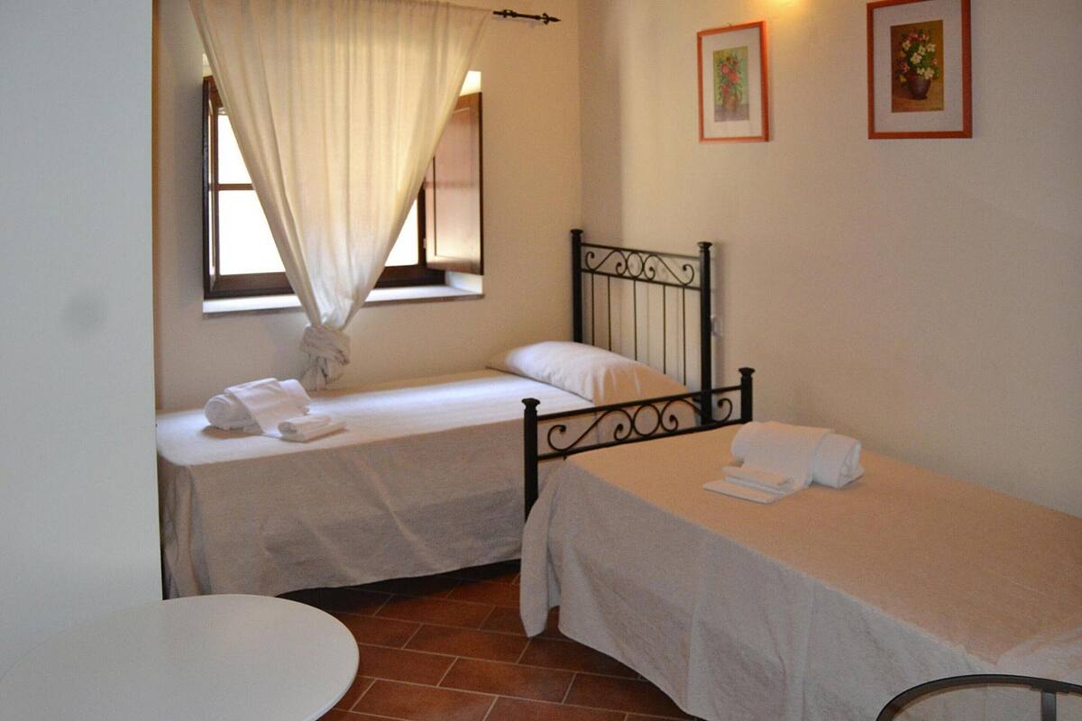 Ein Zimmer mit zwei Einzelbetten, einem runden Tisch und einem Fenster mit Vorhängen.