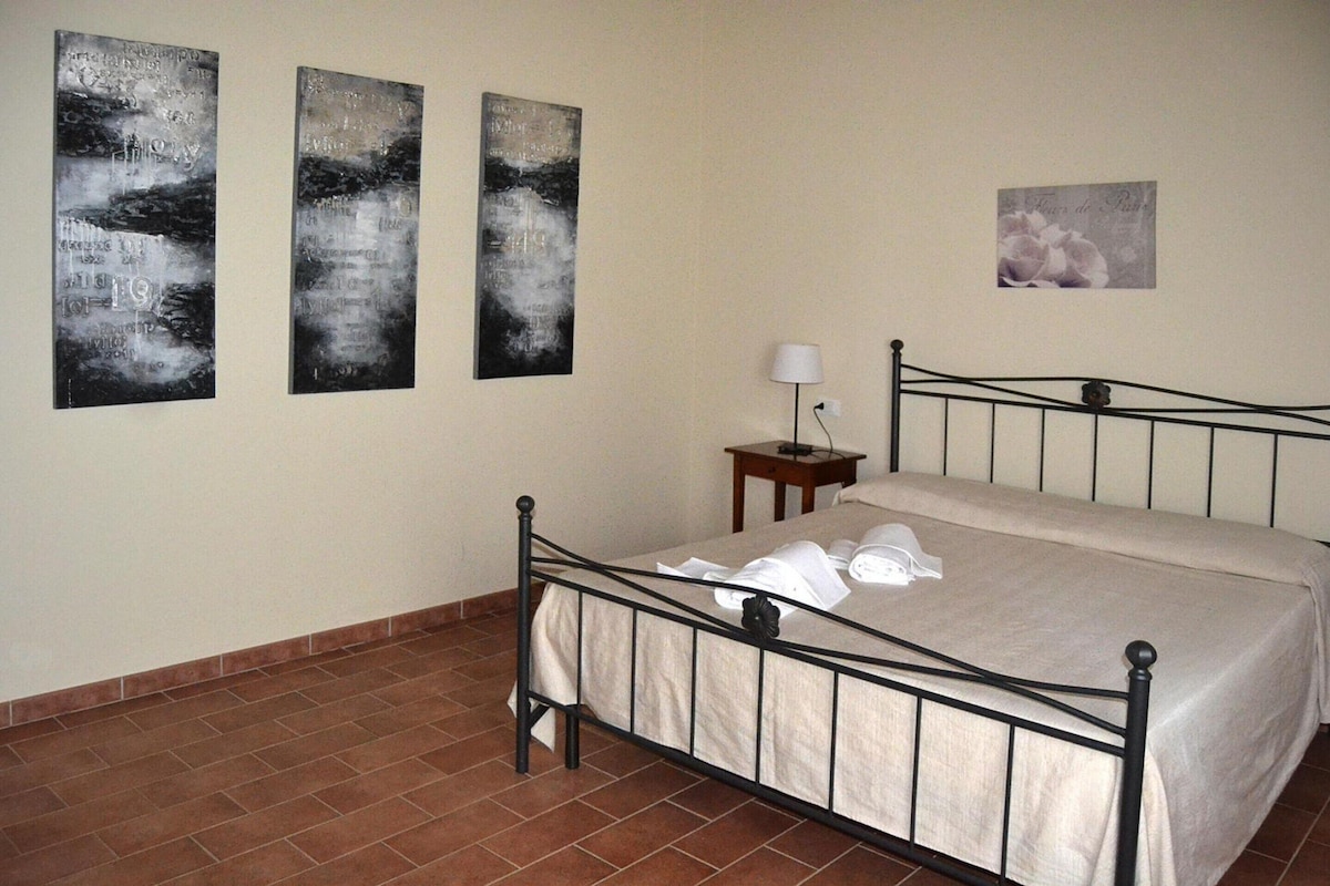 Une chambre à coucher avec un lit en métal, une table de chevet avec une lampe et trois tableaux abstraits accrochés au mur.