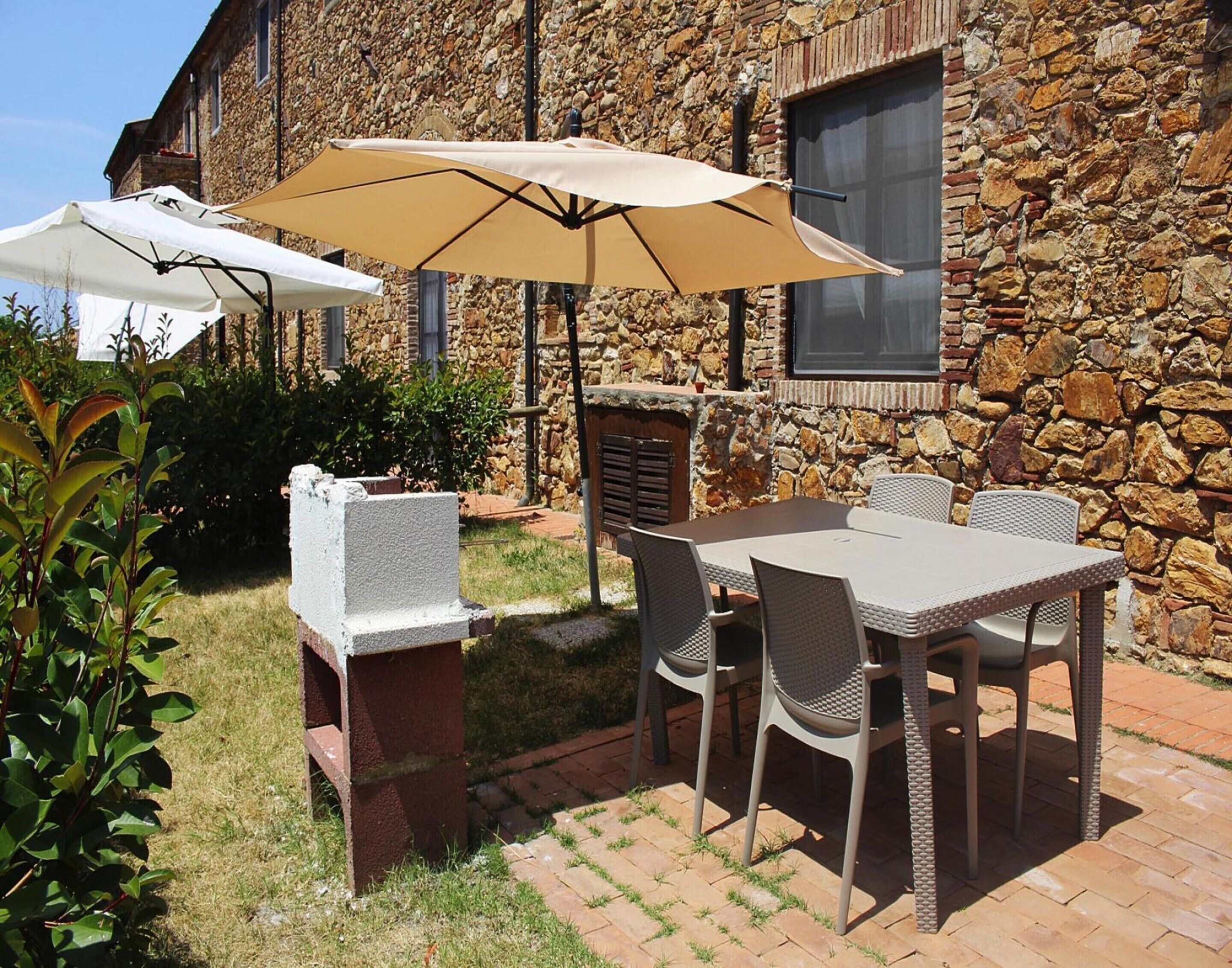 An outdoor patio with a stone wall, a grill, and a table with chairs.