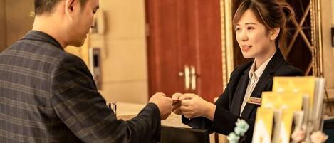 A man and a woman at a reception desk in a hotel lobby with a red door and a vase of flowers.