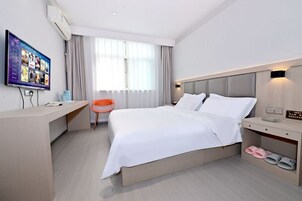 Habitación de hotel con cama, escritorio, silla, televisor y pantuflas.