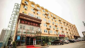 A multi-story hotel with a prominent entrance, a red carpet leading to the doors, and a parking lot with several cars.