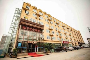 Um hotel com vários andares, entrada imponente, tapete vermelho até as portas e estacionamento com diversos carros.