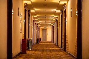 A hotel hallway with doors on both sides, a carpeted floor, and a light fixture on the ceiling. - Royal Hotel (Zhongmu)