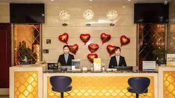 A hotel reception area with a counter, two bar stools, and a wall with clocks and heart-shaped decorations.