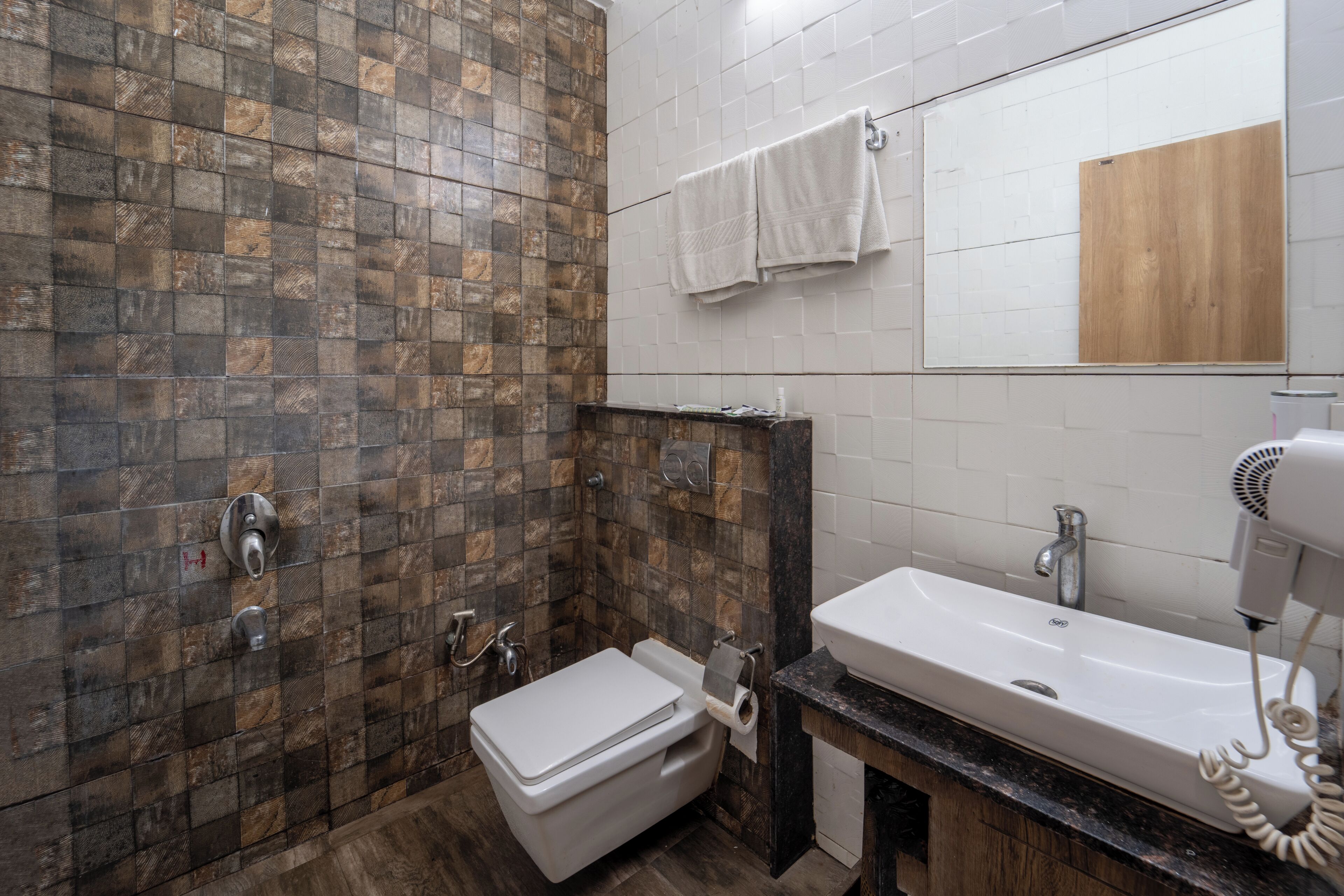 A bathroom with a tiled shower wall, a toilet, a sink with a mirror, and a hairdryer on the counter.