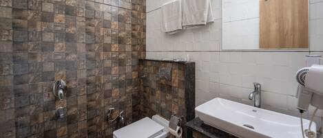 A bathroom with a tiled shower wall, a toilet, a sink with a mirror, and a hairdryer on the counter.