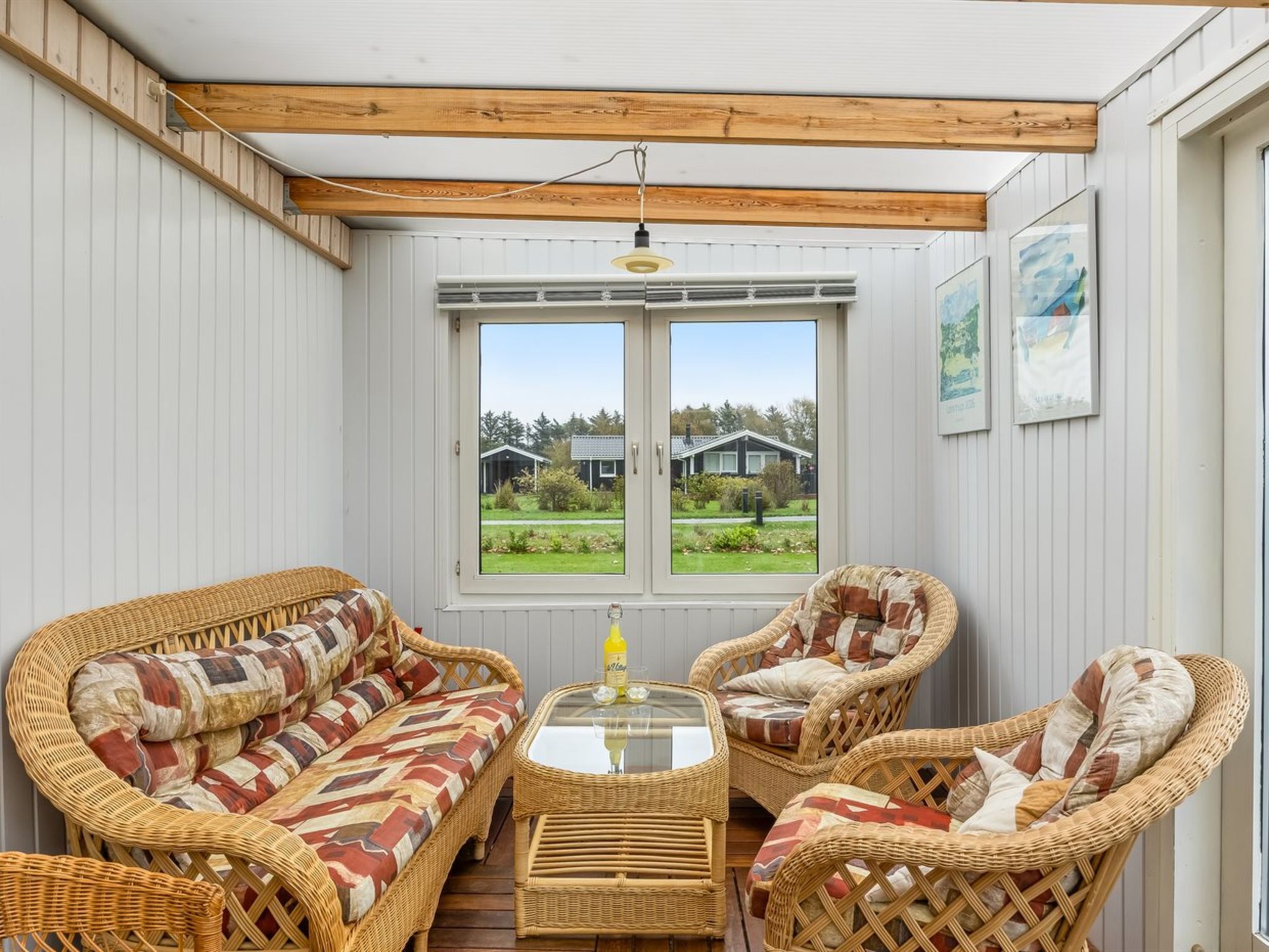 A covered patio with wicker furniture, a glass table, and a view of houses through a window.