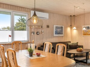 Une pièce chaleureuse avec une table à manger en bois, des chaises, un canapé et une petite table ronde sur laquelle sont disposés des fruits.