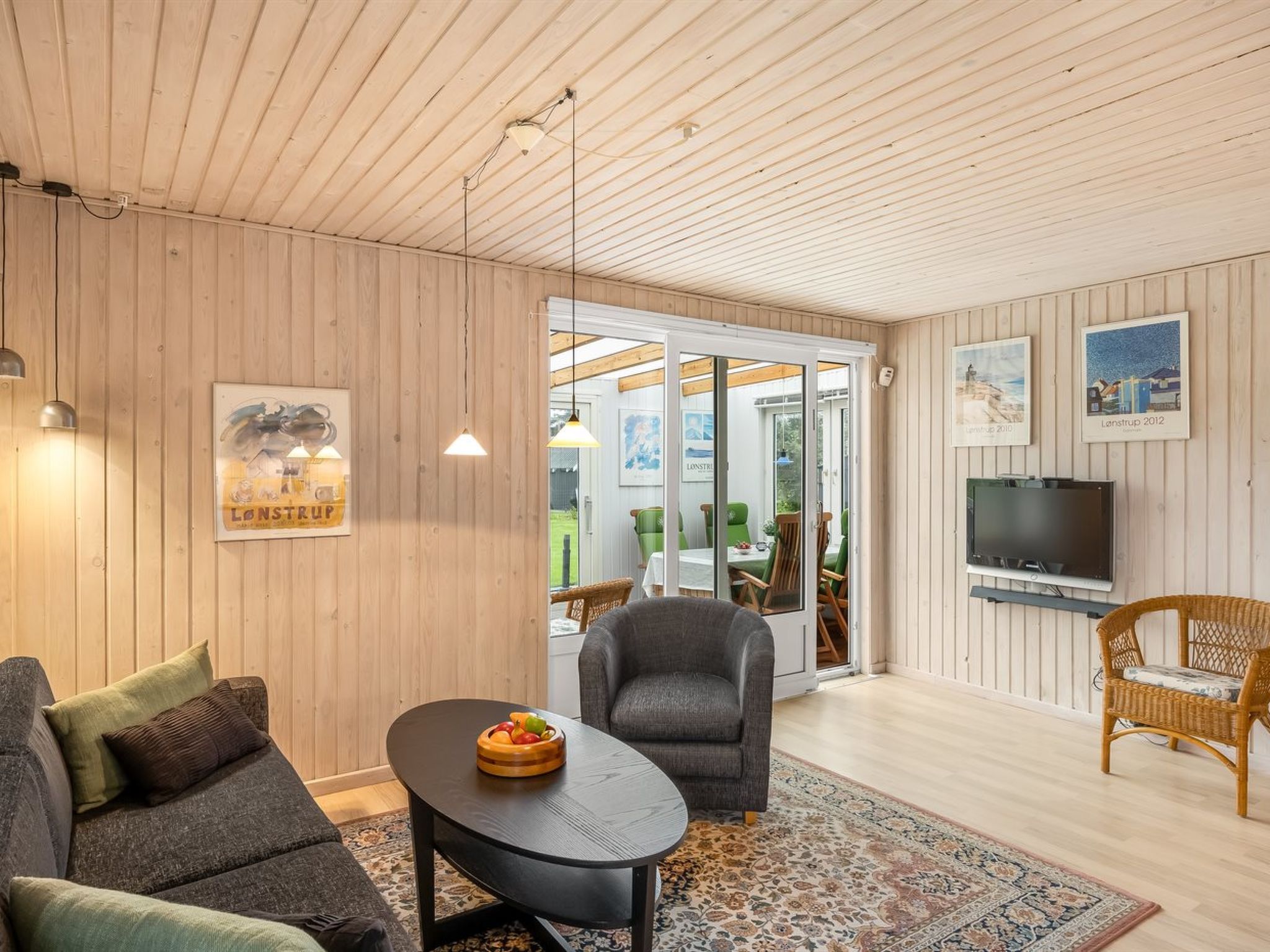 A modern living room with a wooden ceiling, a television, and a dining area with a table and chairs.
