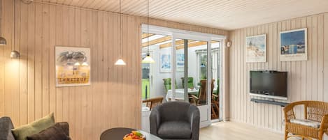 Un salon moderne avec un plafond en bois, un téléviseur et un coin repas comprenant une table et des chaises.