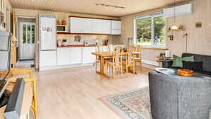 Eine moderne Küche mit weißen Schränken, ein Essbereich mit Holzsesseln und ein graues Sofa in einem geräumigen Wohnzimmer mit Holzboden.