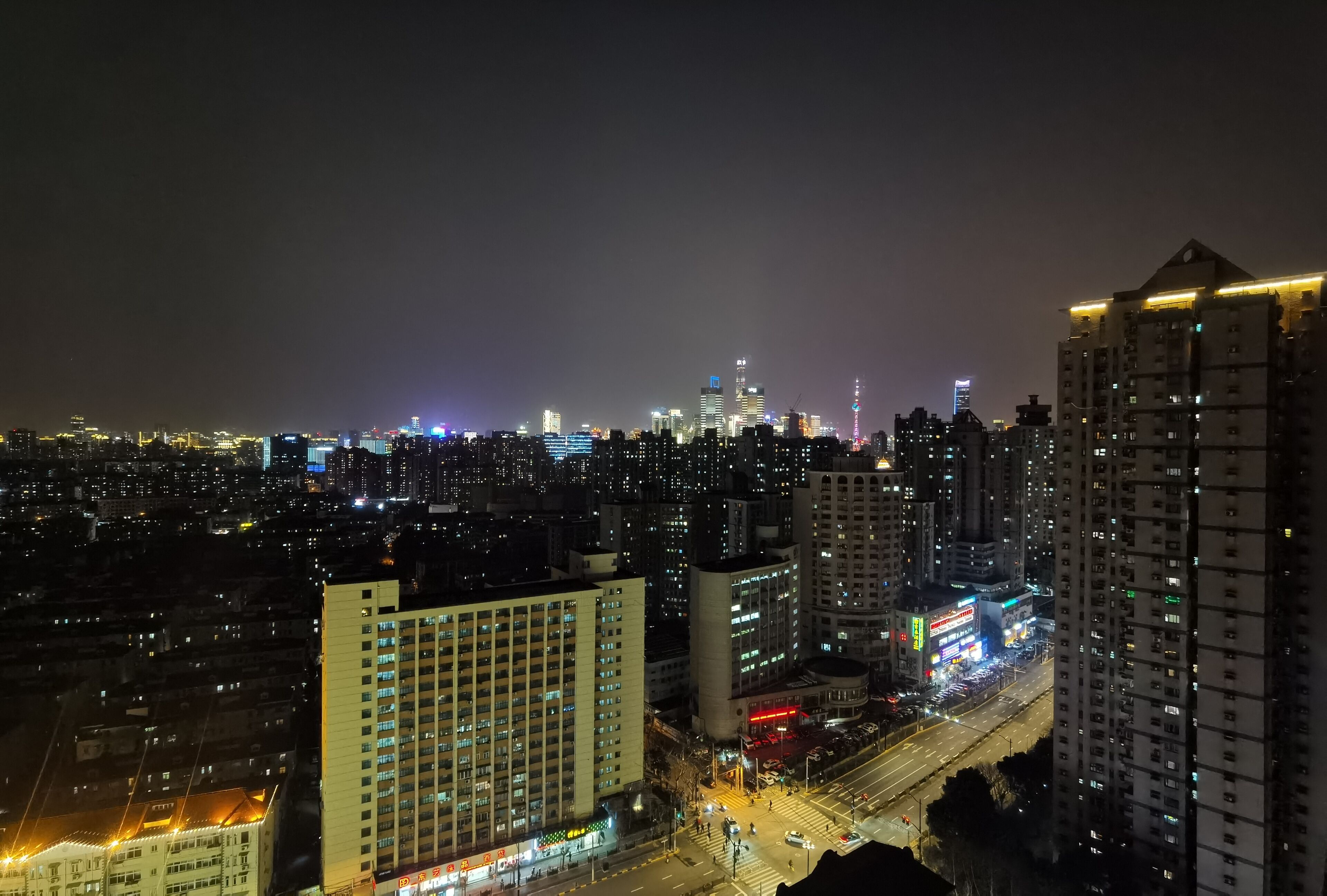 Une vue nocturne d’une ville, avec ses gratte-ciel, ses rues illuminées et un carrefour très fréquenté.