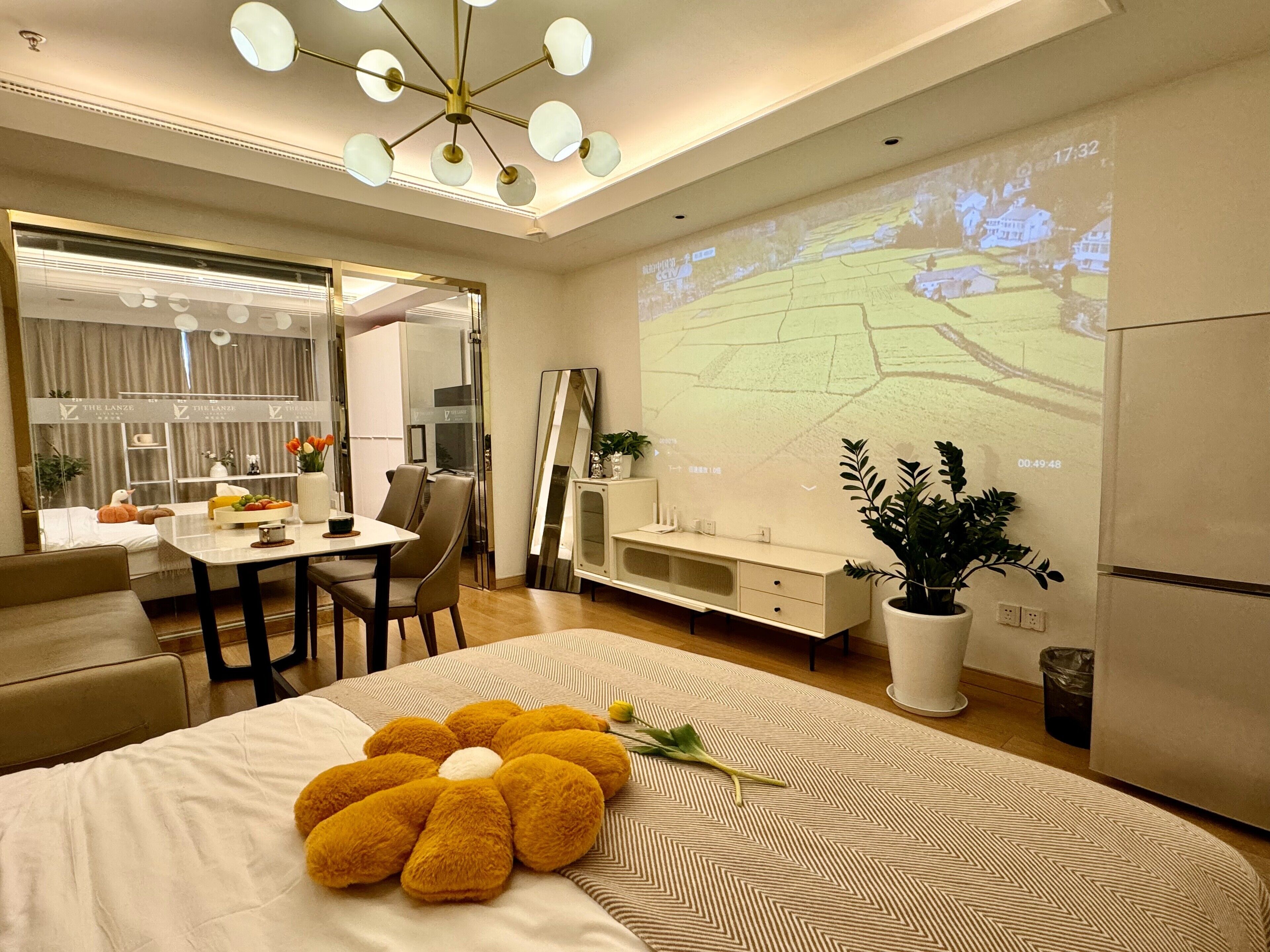 Une chambre d’hôtel moderne dotée d’un grand lit, d’un coin repas, d’un écran de télévision diffusant un paysage et d’un luminaire au plafond.