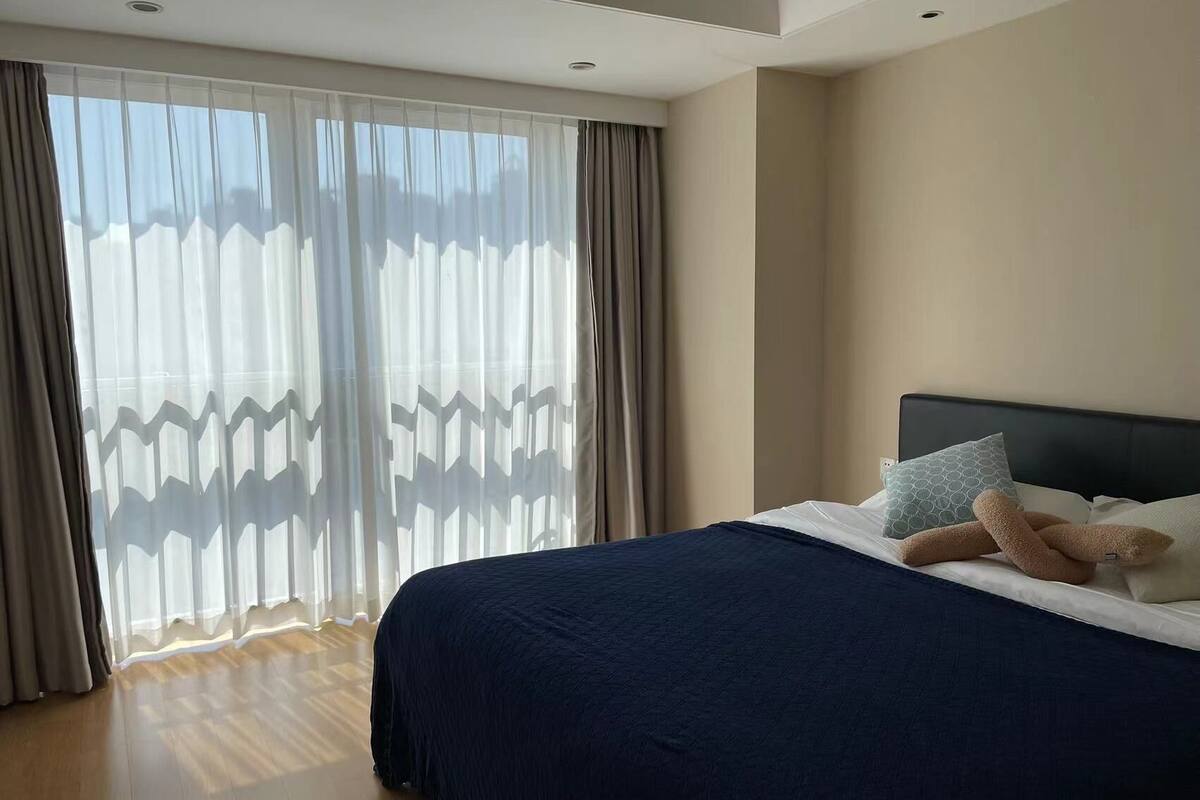 Une chambre d’hôtel avec un grand lit, une tête de lit et une vue à travers des rideaux transparents.