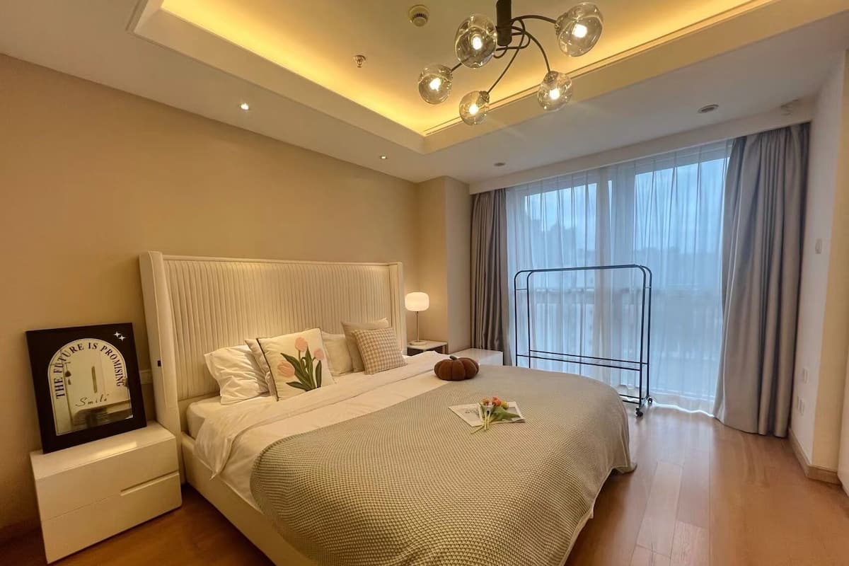 Une chambre à coucher moderne avec un grand lit, des tables de chevet, une commode, une horloge murale et une fenêtre avec des rideaux.