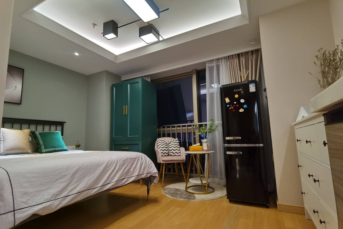 Une chambre moderne comprenant un lit, une petite table, une chaise, un réfrigérateur et une armoire.