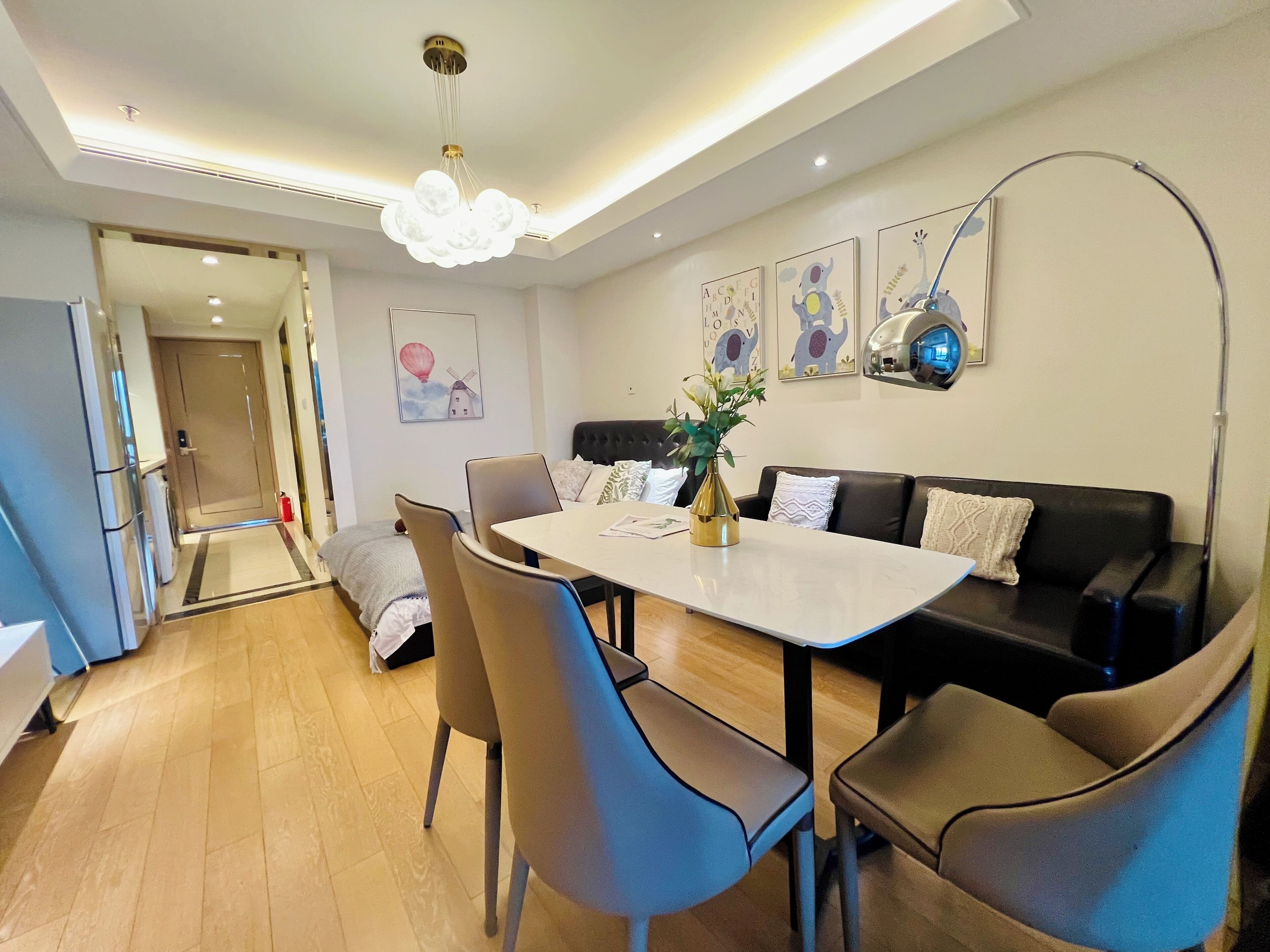 A modern dining area with a white table, brown chairs, and a black sofa. There is a decorative vase on the table, and artwork on the walls.