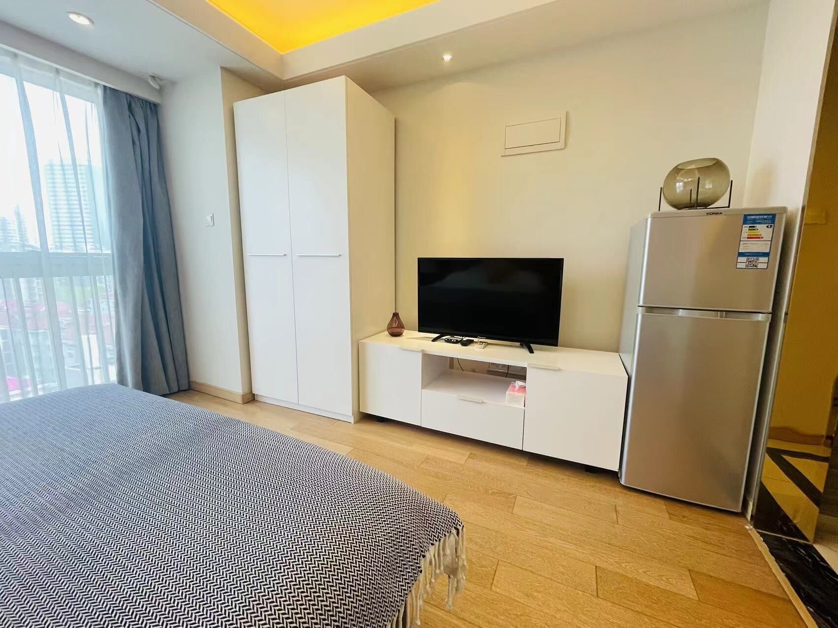 A hotel room with a bed, a TV, a minibar, and a refrigerator.