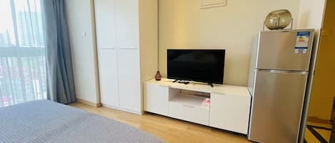 A hotel room with a bed, a TV, a minibar, and a refrigerator.