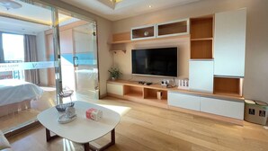 Een moderne hotelkamer met een grote flatscreen-tv, houten planken, een glazen deur naar een balkon en een witte salontafel.