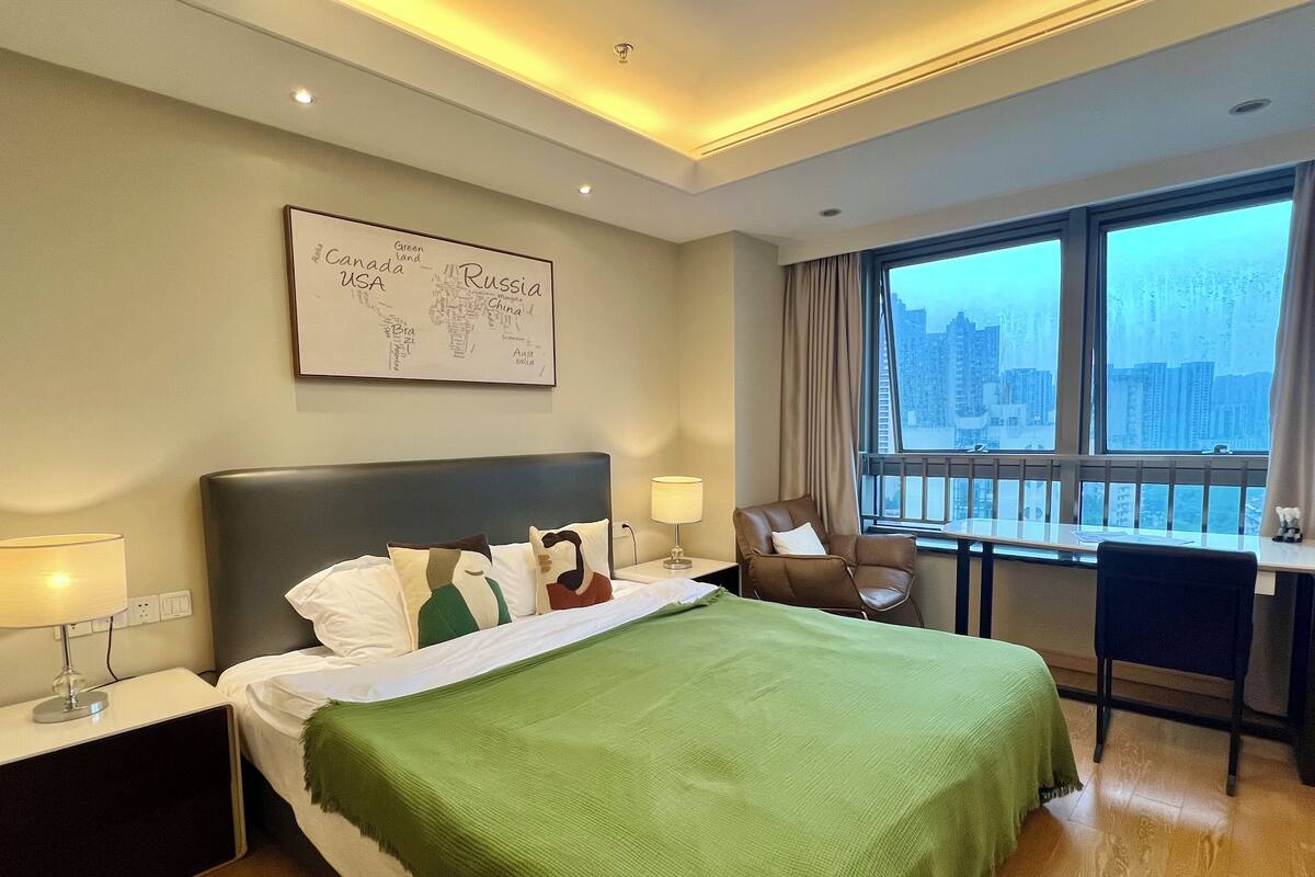 Une chambre d’hôtel comprenant un lit, un bureau, une chaise, une fenêtre donnant sur la ville et une carte géographique murale.