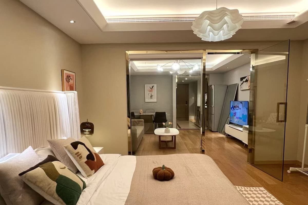 Une chambre d’hôtel moderne dotée d’un grand lit, d’une paroi en verre, d’une télévision et d’un coin repas visible à travers la paroi.