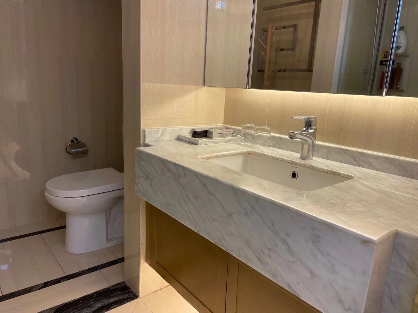 A modern bathroom with a white toilet, a marble sink, and a large mirror.