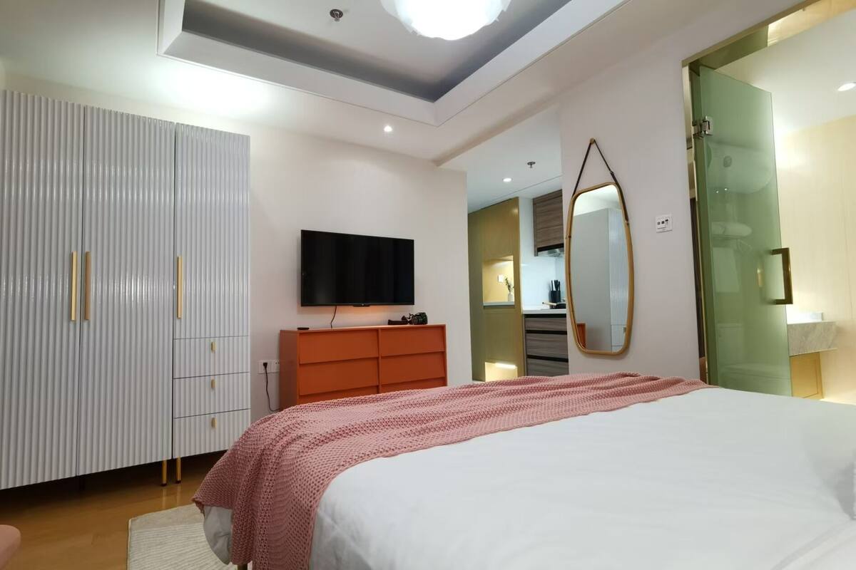 Une chambre à coucher comprenant un lit, une télévision, une armoire, un miroir et une porte menant à la salle de bain.