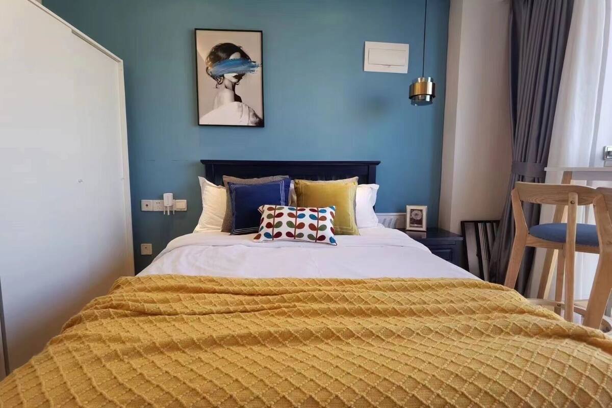 Une chambre d’hôtel avec un lit, une tête de lit, une table de chevet, une chaise et un tableau au mur.