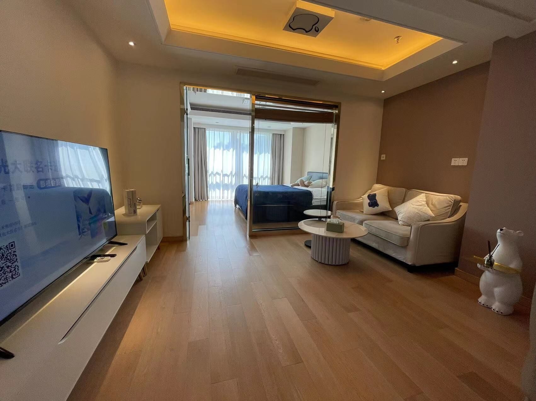 A modern hotel room with a flat-screen TV, a sofa, a coffee table, and a bed with a blue bedspread.