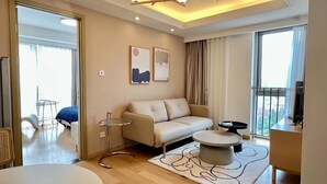 Een moderne woonkamer met een bank, een rond salontafeltje en een televisie. Er is een balkon met uitzicht, en de kamer heeft een groot raam.