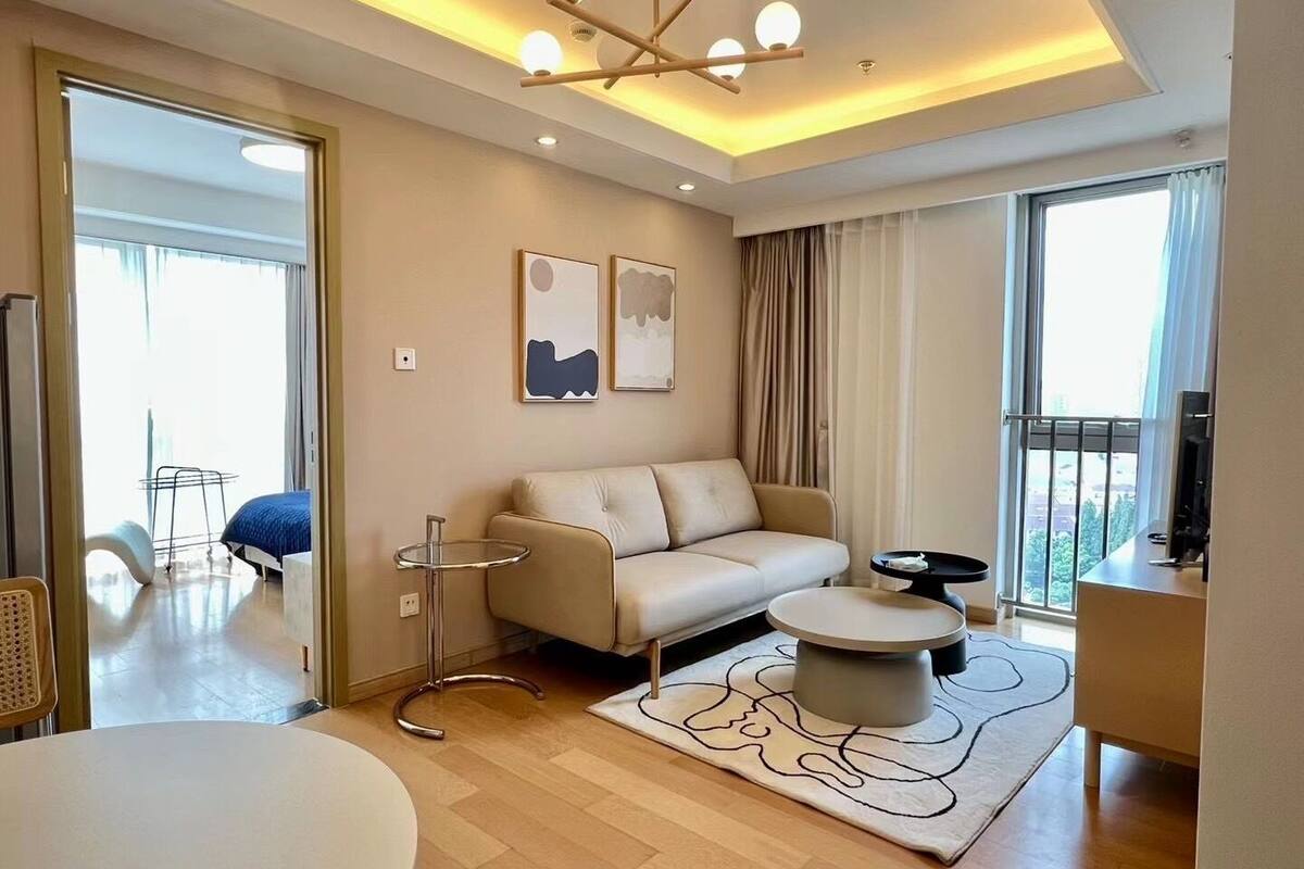 Un salon moderne avec un canapé, une table basse ronde et un téléviseur. Il y a un balcon avec vue, et la pièce est dotée d’une grande fenêtre.
